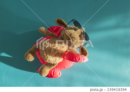 Knitted Plush Sheep in Sunglasses on Pink Pool Flamingo Float Against Blue Water. Knitted Plush Sheep in Sunglasses on Pink Pool Flamingo Float Against Blue Water. 139418394