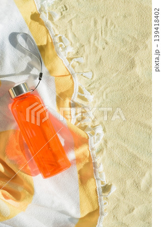 Orange Kid Water Bottle on Beach Towel and Sand. Orange Kid Water Bottle on Beach Towel and Sand. 139418402
