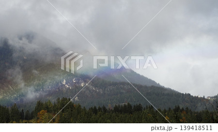 Rainbow arc over a foggy mountain landscape with clouds in the Austrian Alps, suitable as a calm wallpaper or background. Rainbow arc over a foggy mountain landscape with clouds in the Austrian Alps, suitable as a calm wallpaper or background. 139418511