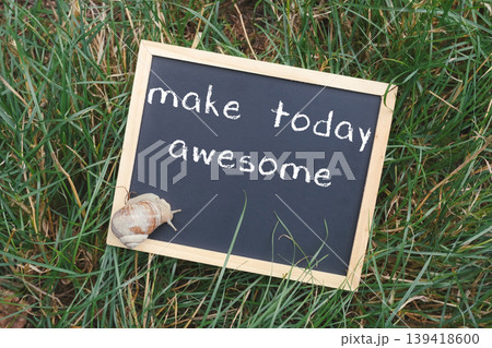 Chalkboard sign with inspiring message surrounded by lush green grass and a decorative snail shell, conveying a positive and motivational atmosphere for daily encouragement 139418600