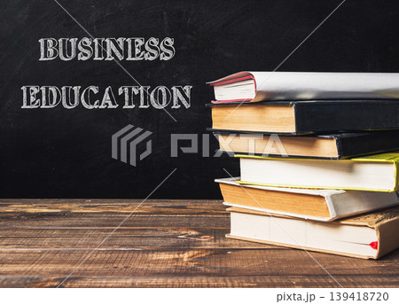 Stack of books on wooden table with chalkboard background featuring business education concepts Stack of books on wooden table with chalkboard background featuring business education concepts 139418720