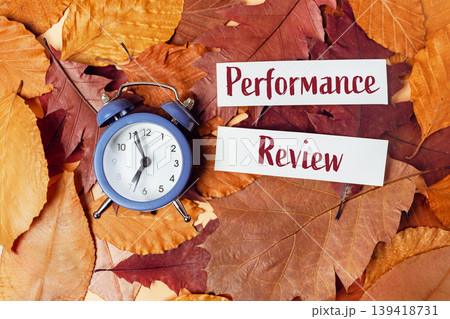 Blue alarm clock placed on autumn leaves with performance review notes, symbolizing time management and evaluation in business and finance settings Blue alarm clock placed on autumn leaves with performance review notes, symbolizing time management and evaluation in business and finance settings 139418731
