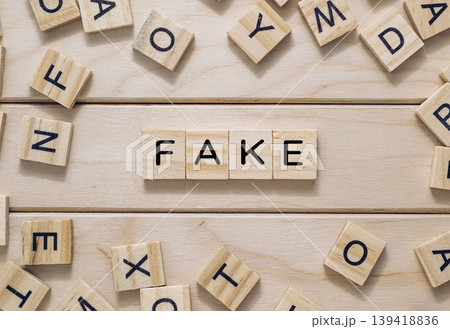 Wooden letter tiles spelling the word fake surrounded by scattered letters on a wooden surface 139418836