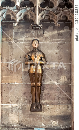 Bronze statue of a young knight in armor standing against a textured stone wall, showcasing historical craftsmanship and medieval artistry Bronze statue of a young knight in armor standing against a textured stone wall, showcasing historical craftsmanship and medieval artistry 139418885