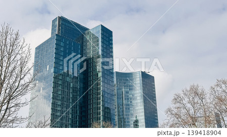 Modern glass skyscrapers reflecting clouds and trees in a vibrant urban environment Modern glass skyscrapers reflecting clouds and trees in a vibrant urban environment 139418904