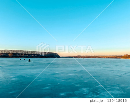 Frozen river landscape with people fishing under a clear blue sky during winter season 139418916