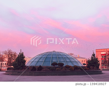 Glass dome structure surrounded by greenery and trees, under a colorful sky at dusk, showcasing modern architecture and serene atmosphere 139418927