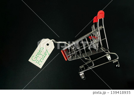 Shopping cart with red handles and a tag reading Green Friday, symbolizing sales and discounts, set against a dark background, emphasizing retail excitement and consumerism Shopping cart with red handles and a tag reading Green Friday, symbolizing sales and discounts, set against a dark background, emphasizing retail excitement and consumerism 139418935