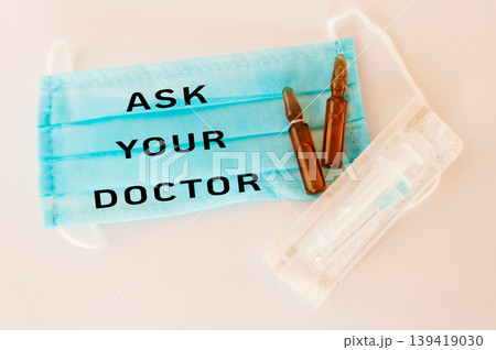 Medical mask with text, vials, and syringe on a clean surface for healthcare awareness 139419030