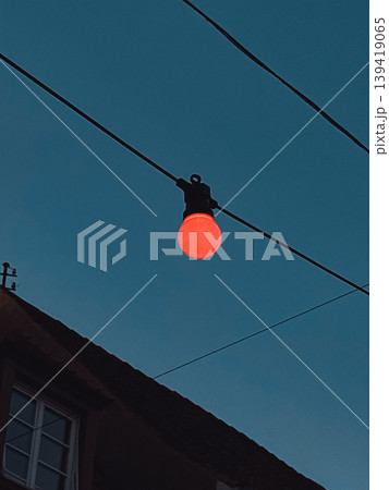 Red light bulb hanging from wire against a twilight sky illuminating urban atmosphere Red light bulb hanging from wire against a twilight sky illuminating urban atmosphere 139419065