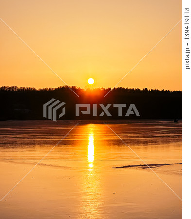 Sunset over tranquil lake reflecting golden hues with silhouettes of trees in the background Sunset over tranquil lake reflecting golden hues with silhouettes of trees in the background 139419118