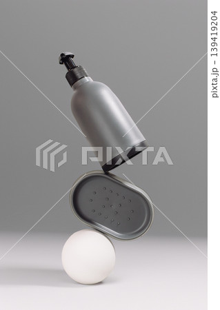 Gray cosmetic bottle and container balanced on a white sphere against a minimalist background Gray cosmetic bottle and container balanced on a white sphere against a minimalist background 139419204