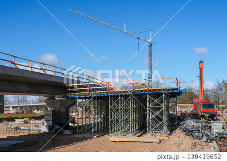 Bridge construction site with tower crane scaffolding and red mobile crane under blue sky view Bridge construction site with tower crane scaffolding and red mobile crane under blue sky view 139419652