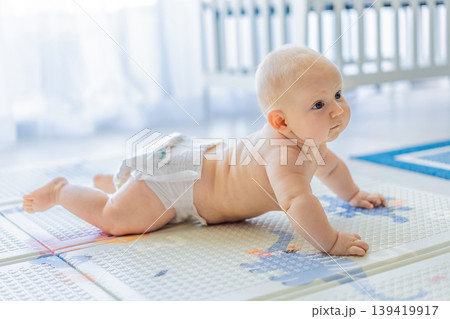 Baby lying on play mat learning to crawl and get on all fours. Infant practicing motor skills and development at home. Early childhood growth, milestones and active learning concept Baby lying on play mat learning to crawl and get on all fours. Infant practicing motor skills and development at home. Early childhood growth, milestones and active learning concept 139419917