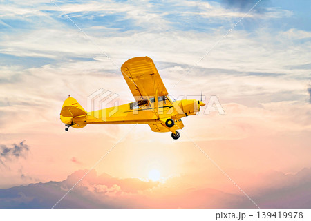 Single engine ultralight airplane flying under an orange sky at sunset Single engine ultralight airplane flying under an orange sky at sunset 139419978