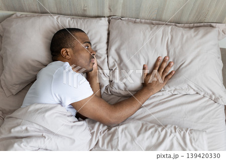 African american man lying awake in bed looking sideways at empty space African american man lying awake in bed looking sideways at empty space 139420330