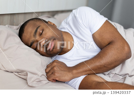 Black man in white tshirt sleeping peacefully on his side in bed Black man in white tshirt sleeping peacefully on his side in bed 139420337