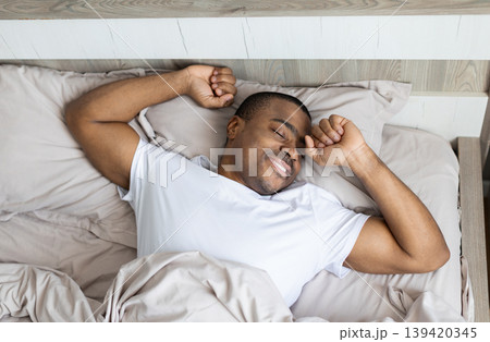 African american man sleeping comfortably on bed with arms relaxed in bedroom African american man sleeping comfortably on bed with arms relaxed in bedroom 139420345
