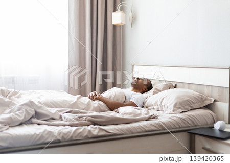 African american man lying on bed looking upward in bedroom African american man lying on bed looking upward in bedroom 139420365
