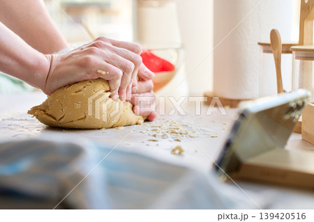 Hands kneading dough on floured kitchen surface near smartphone 139420516