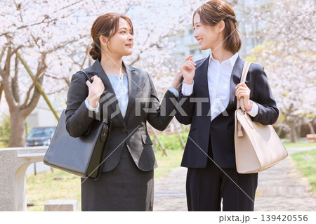 桜並木の下で会話する二人のスーツ姿の新入社員の女性・春の入社式イメージ 139420556