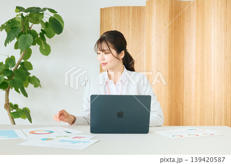オフィスでノートパソコンと資料を使いデータ分析をする若い女性ビジネスパーソン・白スーツ姿の会社員 オフィスでノートパソコンと資料を使いデータ分析をする若い女性ビジネスパーソン・白スーツ姿の会社員 139420587
