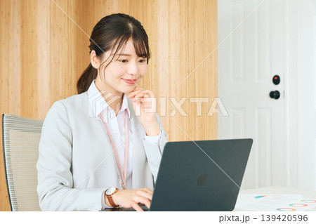 オフィスでノートパソコンを操作する若い女性ビジネスパーソン・笑顔でPC作業をするスーツ姿の会社員 139420596