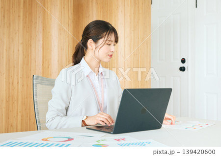 オフィスでノートパソコンと資料を使い業務に取り組む若い女性ビジネスパーソン・スーツ姿の会社員 オフィスでノートパソコンと資料を使い業務に取り組む若い女性ビジネスパーソン・スーツ姿の会社員 139420600