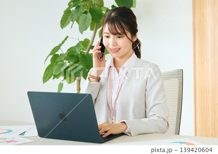 オフィスでスマートフォンで通話しながらノートパソコンを操作する若い女性ビジネスパーソン・スーツ姿の会 オフィスでスマートフォンで通話しながらノートパソコンを操作する若い女性ビジネスパーソン・スーツ姿の会 139420604