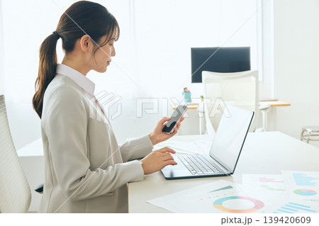 オフィスでスマートフォンとノートパソコンを使って仕事をする若い女性ビジネスパーソン・会社員のデスクワ オフィスでスマートフォンとノートパソコンを使って仕事をする若い女性ビジネスパーソン・会社員のデスクワ 139420609