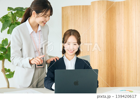 オフィスでノートパソコンを見ながら打ち合わせをする二人の若い女性ビジネスパーソン・先輩社員が後輩に指 139420617