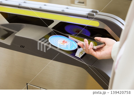 駅の自動改札機にスマートフォンをタッチして通過する手元・モバイルIC乗車券で電車に乗る様子 駅の自動改札機にスマートフォンをタッチして通過する手元・モバイルIC乗車券で電車に乗る様子 139420758