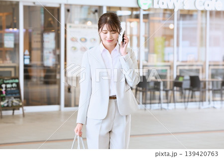 カフェの前でスマートフォンで通話しながら歩くスーツ姿の若い女性ビジネスパーソン カフェの前でスマートフォンで通話しながら歩くスーツ姿の若い女性ビジネスパーソン 139420763