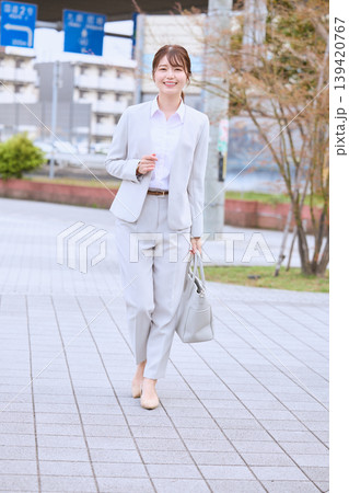 春の街中を歩く白いスーツ姿の若い女性ビジネスパーソン・笑顔で通勤する日本人女性会社員 139420767