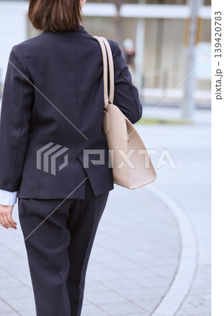 ビジネスバッグを肩にかけて歩く紺スーツ姿の女性ビジネスパーソンの後ろ姿・就職活動イメージ 139420783