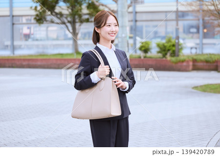 ベージュのバッグを持ち屋外を歩くスーツ姿の若い日本人女性ビジネスパーソン・就職活動・通勤イメージ ベージュのバッグを持ち屋外を歩くスーツ姿の若い日本人女性ビジネスパーソン・就職活動・通勤イメージ 139420789