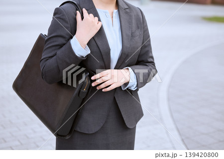 ビジネスバッグを持って屋外を歩くスーツ姿の女性ビジネスパーソン・グレーのスーツと水色ブラウスの通勤イ ビジネスバッグを持って屋外を歩くスーツ姿の女性ビジネスパーソン・グレーのスーツと水色ブラウスの通勤イ 139420800