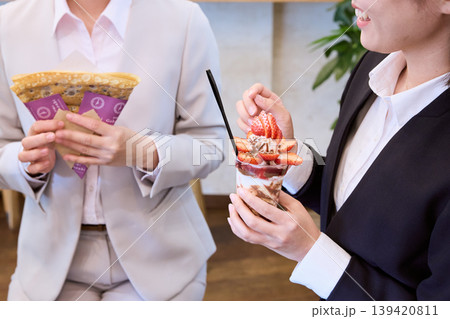 カフェでクレープとストロベリーパフェを持つスーツ姿の女性二人・ビジネスウーマンのランチタイム カフェでクレープとストロベリーパフェを持つスーツ姿の女性二人・ビジネスウーマンのランチタイム 139420811