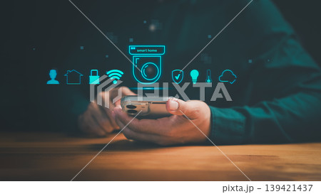 Smart home automation system with security camera and mobile control. Hand holding smartphone for IoT house protection, monitoring, and remote wireless technology. 139421437