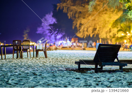 Two wooden beach loungers on white sand under lush trees at night on Koh Rong Cambodia 139421660
