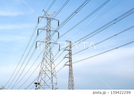 High-voltage electricity transmission towers and power lines against a bright blue sky. Industrial infrastructure for electric energy distribution and power supply systems in clear outdoor setting. High-voltage electricity transmission towers and power lines against a bright blue sky. Industrial infrastructure for electric energy distribution and power supply systems in clear outdoor setting. 139422299