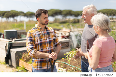Elderly couple and young man talking together on farm field 139422682