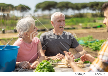 Young man and elderly couple sitting at table with harvest on field Young man and elderly couple sitting at table with harvest on field 139422693