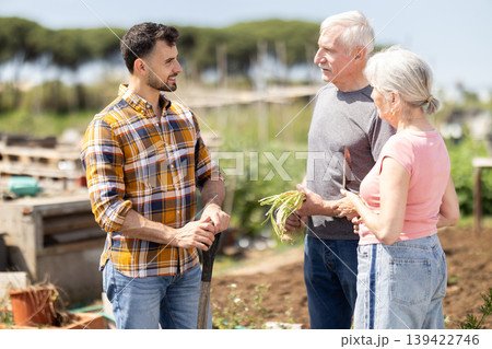 Elderly couple and young man talking together on farm field Elderly couple and young man talking together on farm field 139422746