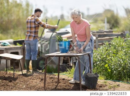Mature woman works in the garden outdoors - preparing various tools for caring for plants Mature woman works in the garden outdoors - preparing various tools for caring for plants 139422833