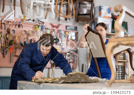 Male and female carpenters working on restoring vintage mirror and chair in workshop Male and female carpenters working on restoring vintage mirror and chair in workshop 139423173