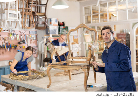 Skilled middle-aged male furniture repair specialist in uniform restoring Victorian chair during workday in workshop 139423293