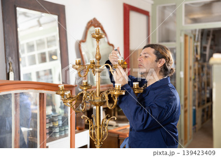 Man restorer with brush removes dirt and dust deposits from bedside antique floor lamp Man restorer with brush removes dirt and dust deposits from bedside antique floor lamp 139423409
