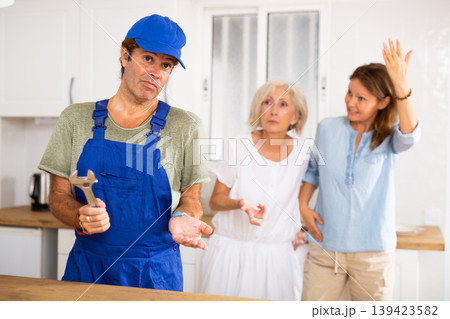 Inept plumber throws up his hands. In background, disgruntled apartment owners scold him Inept plumber throws up his hands. In background, disgruntled apartment owners scold him 139423582