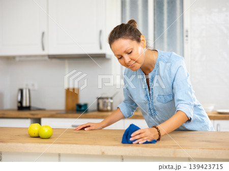 Focused woman cleaning kitchen table at home Focused woman cleaning kitchen table at home 139423715